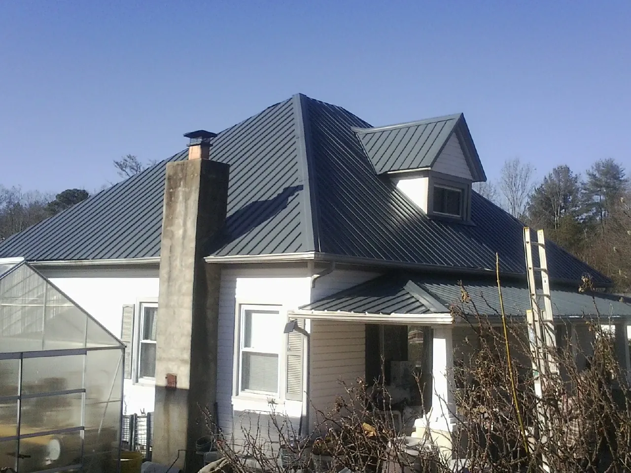 Dark blue standing seam metal roof on a white farmhouse with dormer — Slate & Tile Roof Repair by Roofing Brothers in Whites Creek