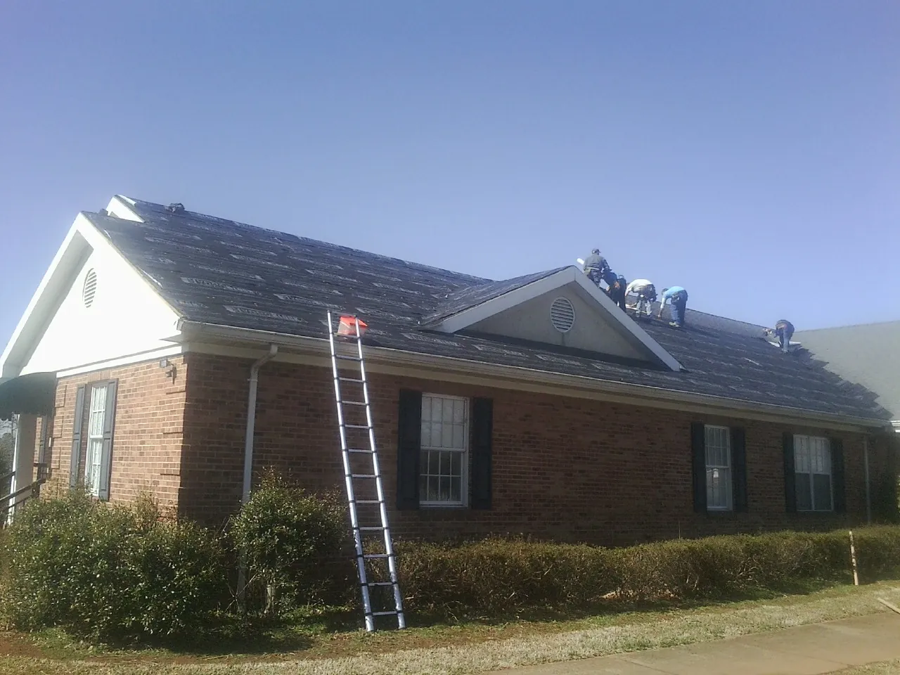 Crew tearing shingles off a brick ranch roof with a ladder set — Metal Roof Repair work by our crew in Whites Creek