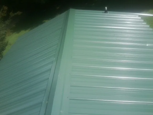 New green metal panels meeting at the ridge of a roof — Flat Roof Repair work by our crew in Whites Creek