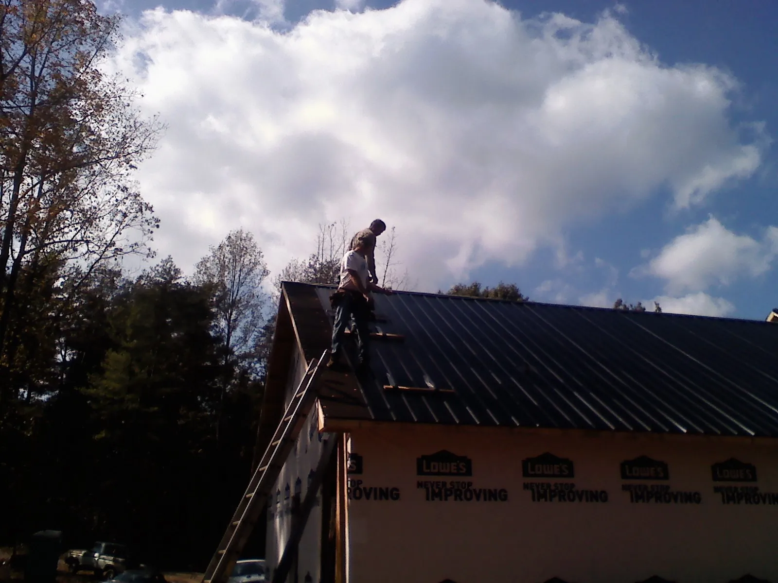 Roofer fastening dark metal panels high against a cloudy sky, from a Roof Inspection job in Whites Creek