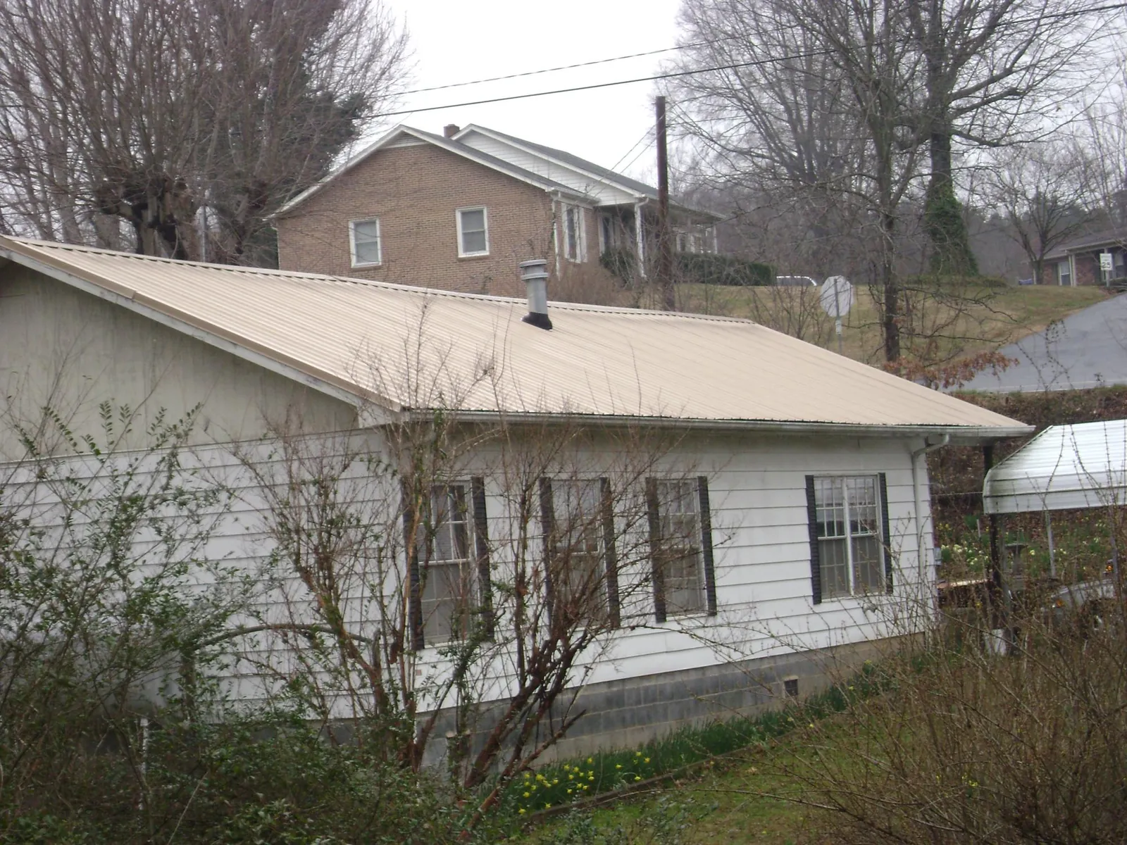 Tan metal roof on a white sided house set into a hillside — Commercial Roofing by Roofing Brothers in Whites Creek