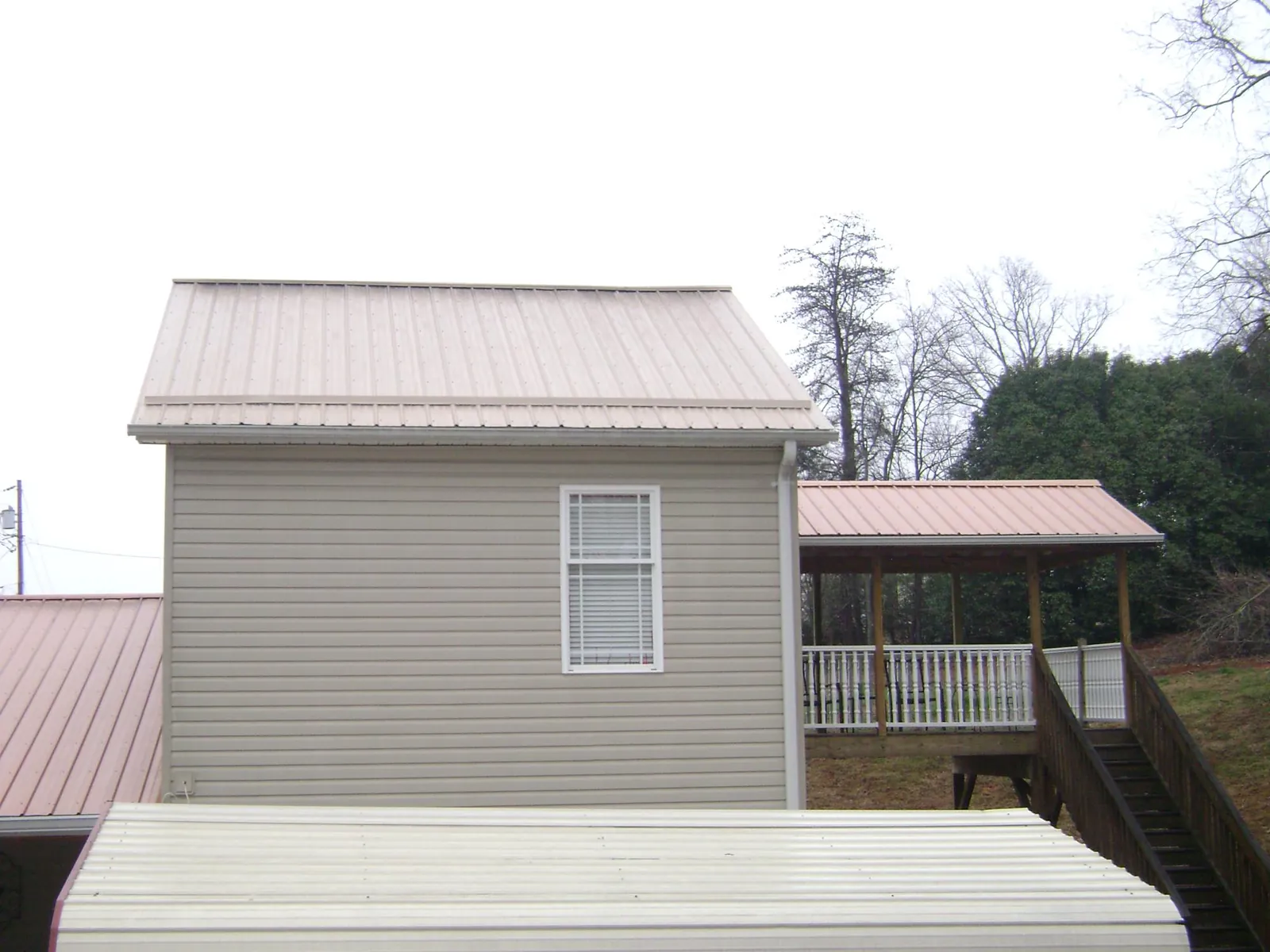Tan metal roofs on a two story addition and attached porch, from a Roof Replacement job in Whites Creek